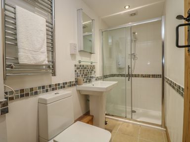 A bathroom with a toilet sink mirror and glass shower enclosure at Barneys Barn in Sennen