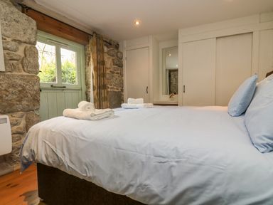 A bedroom with a bed with light blue bedding folded towels on the bed stone walls and a window at Barneys Barn in Sennen