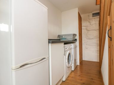 A utility room with a white fridge freezer washing machine dryer and a laundry basket on the counter at Barneys Barn in Sennen