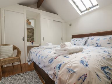 A bedroom with a bed with nautical themed bedding towels on the bed a wicker chair and built in wardrobes at Barneys Barn in Sennen