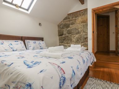 A bedroom with a bed covered in sailboat patterned bedding towels on the bed exposed stone wall and wooden door at Barneys Barn in Sennen