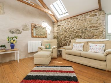 A living room with beige sofa and armchair a striped rug and a side table with flowers at Barneys Barn in Sennen