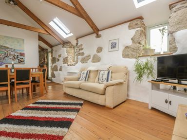 A living room with a beige sofa and dining table with chairs on wooden floor at Barneys Barn in Sennen