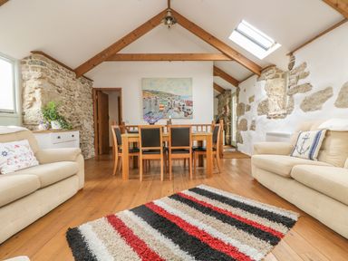 A living room with wooden floor beams stone walls a dining table with chairs and sofas at Barneys Barn in Sennen