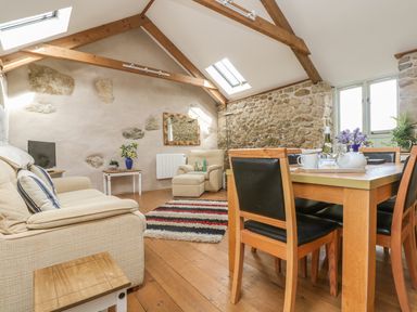 A living room with wooden beams stone walls sofa armchair dining table and chairs at Barneys Barn in Sennen