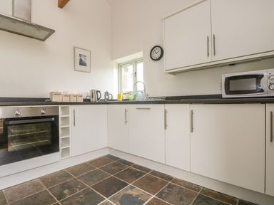 A kitchen with white cabinets a built in oven a microwave a kettle and labeled canisters at Barneys Barn in Sennen