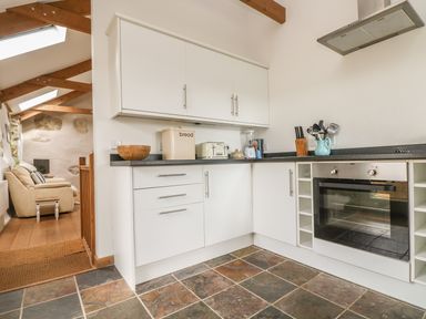 A kitchen with white cabinets oven and countertop appliances next to a living area with beige sofa at Barneys Barn in Sennen