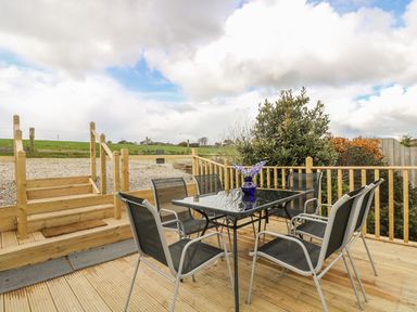 An outdoor wooden deck with a glass table surrounded by six metal chairs and lavender in a blue vase on the table at Barneys Barn in Sennen