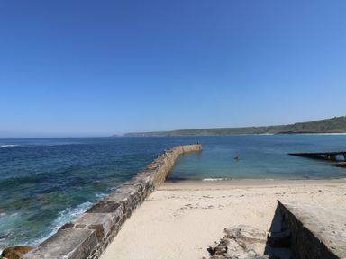 A stone pier extending into the ocean from a sandy beach with hills in the background at Barneys Barn in Sennen