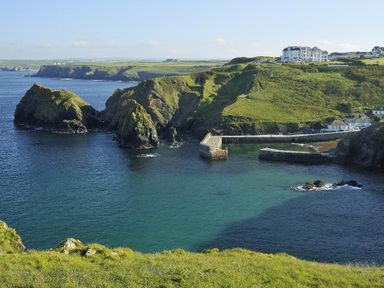 A coastal scene with cliffs green grass a stone pier and buildings on the hillside at Ridgeback House in Mullion