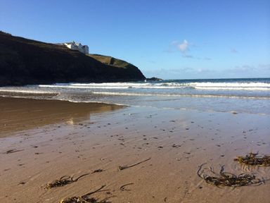 A sandy beach with seaweed and waves near a cliff with a large building on top at Ridgeback House in Mullion