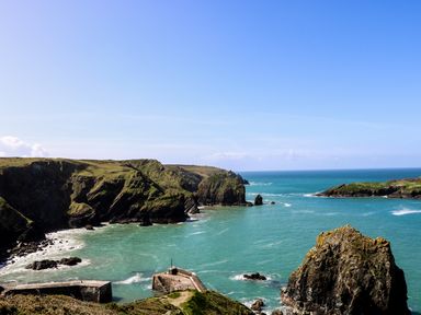 A coastal scene with rocky cliffs and a small stone pier extending into the sea at Ridgeback House in Mullion
