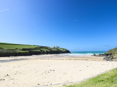 A sandy beach with a grassy hill and a house on top overlooking the ocean at Ridgeback House Mullion