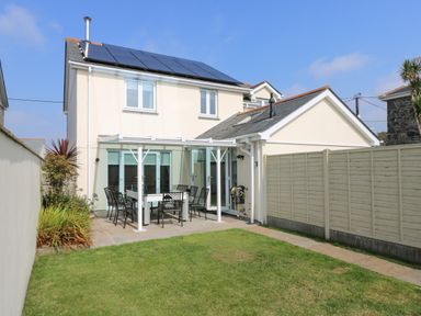 A backyard with a white patio set on a paved area next to a beige house with solar panels on the roof at Ridgeback House in Mullion