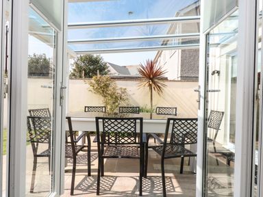A patio dining area with a table and six black lattice chairs under a glass roof at Ridgeback House Mullion