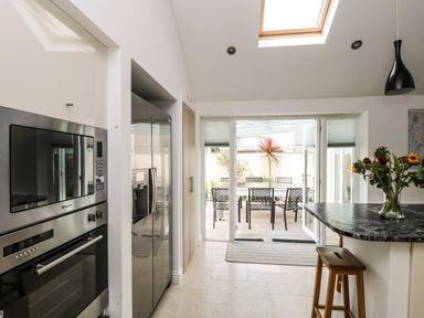 A kitchen with stainless steel appliances and a marble countertop with flowers overlooking a patio with a table and chairs at Ridgeback House in Mullion