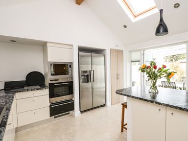 A kitchen with a refrigerator oven microwave island with flowers and doors leading outside at Ridgeback House Mullion