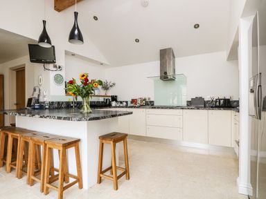 A kitchen with wooden stools around an island and flowers on the counter at Ridgeback House in Mullion