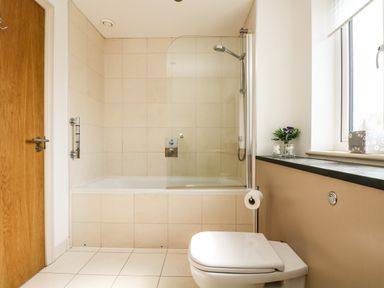 A bathroom with a bathtub shower combination a toilet near a window and a wooden door at Ridgeback House in Mullion
