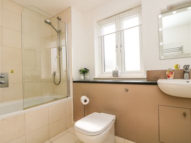 A bathroom with a bathtub shower combo toilet sink mirror window with blinds and flowers on the windowsill at Ridgeback House in Mullion