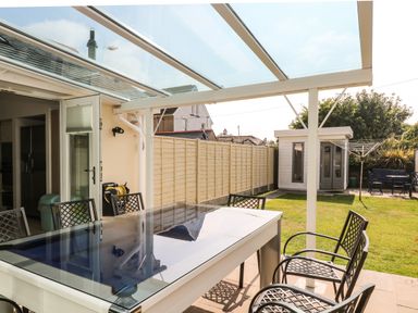 An outdoor covered patio with a table and chairs overlooking a fenced garden with a shed and a clothesline at Ridgeback House in Mullion