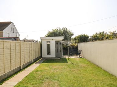 A backyard with a lawn, paved path, wooden shed, clothesline, and outdoor seating area at Ridgeback House in Mullion