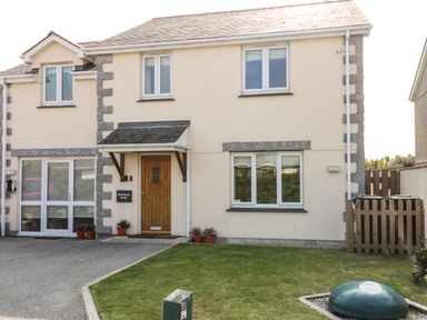 A two-story semi-detached house with a wooden front door and driveway with grass at Ridgeback House in Mullion