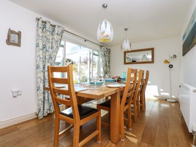 A dining room with a wooden table and chairs next to glass doors and floral curtains at Ridgeback House in Mullion