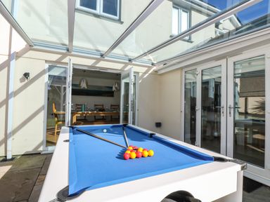 A pool table with blue felt and billiard balls in a glass roofed patio at Ridgeback House in Mullion