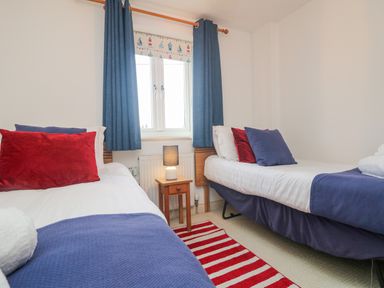 A bedroom with two single beds blue curtains and a striped red and white rug at Ridgeback House in Mullion