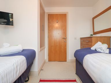 A bedroom with two single beds with towels a dresser with a mirror and a wooden door at Ridgeback House in Mullion