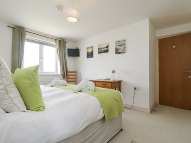 A bedroom with a bed, side table, and window at Ridgeback House, Mullion