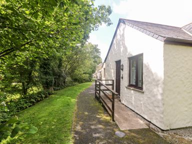 A pathway with a railing alongside a white building and trees and grass on the other side at Tre Pol Pen in Falmouth