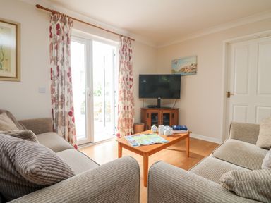 A living room with two beige sofas a wooden coffee table a television on a wooden cabinet and floral curtains at Tre Pol Pen in Falmouth