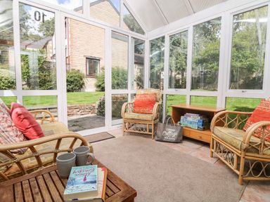 A conservatory with wicker chairs and a wooden table with mugs and books at Tre Pol Pen in Falmouth
