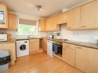 A kitchen with wooden cabinets a washing machine a dishwasher an oven and a window at Tre Pol Pen in Falmouth