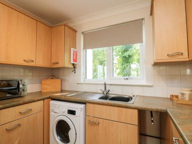 A kitchen with light wood cabinets a washing machine a microwave and a sink under a window at Tre Pol Pen in Falmouth