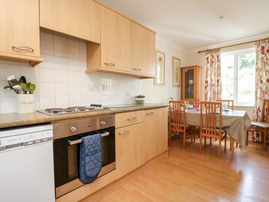 A kitchen with wooden cabinets a dining table with chairs and a window with patterned curtains at Tre Pol Pen in Falmouth