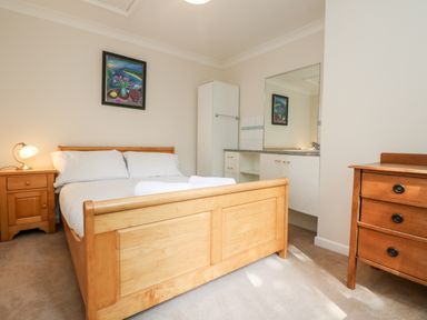 A bedroom with a wooden bed frame, bedside table with lamp, dresser, and a large mirror at Tre Pol Pen in Falmouth