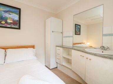 A bedroom with a bed a white cabinet a vanity unit with a sink and a large mirror at Tre Pol Pen in Falmouth