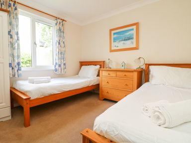 A bedroom with two wooden single beds white bedding a wooden chest of drawers and a window with floral curtains at Tre Pol Pen in Falmouth