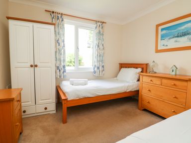 A bedroom with a single bed white wardrobe wooden chest of drawers and a window at Tre Pol Pen in Falmouth