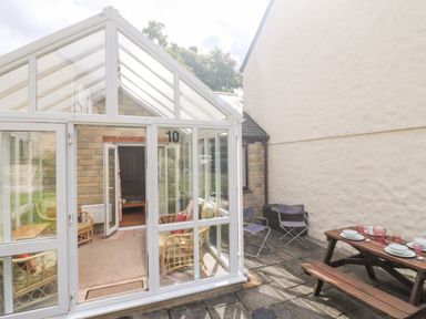 A conservatory with wicker furniture and an outdoor patio with a wooden picnic table set with plates and glasses at Tre Pol Pen in Falmouth