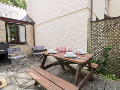 An outdoor patio with a wooden picnic table set with dishes and pink glasses two folding chairs and a barbecue grill at Tre Pol Pen in Falmouth