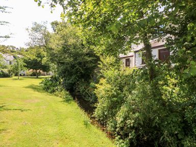 A garden with grass trees bushes a small stream and white houses at Tre Pol Pen in Falmouth