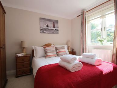 A bedroom with a double bed red bedspread white towels bedside tables with lamps a wardrobe and a window at Speedwell in Charlestown
