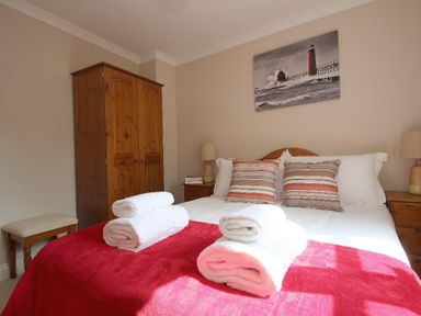 A bedroom with a double bed covered with white sheets and red blanket with rolled white towels a wooden wardrobe two nightstands with lamps and a stool at Speedwell in Charlestown