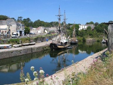 A canal with boats docked alongside a stone walkway with buildings and greenery in the background at Speedwell in Charlestown