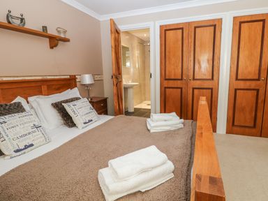 A bedroom with a wooden bed, white towels on a brown blanket, pillows, bedside table with lamp, wooden closet doors, and an open door leading to a bathroom at Speedwell in Charlestown