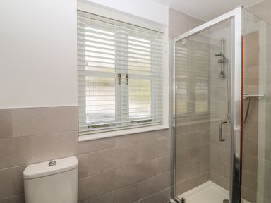 A bathroom with a window with blinds a toilet and a glass shower enclosure with a showerhead at Speedwell in Charlestown